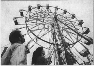 A black and white image featuring a man and a woman look up at a 65 foot tall Eli Bridge Ferris Wheel that is traveling the fairgrounds of the United States. The wheel once belonged to Michael Jackson.